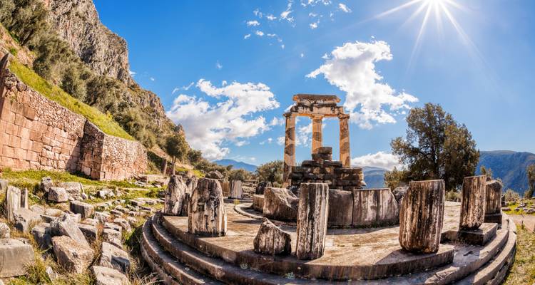 Ruins of the Tholos of Delphi bathed in bright sunlight with mountains in the background