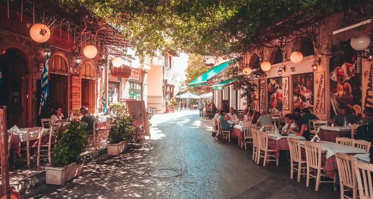Lively shaded street in Athens lined with outdoor tavernas where people dine al fresco