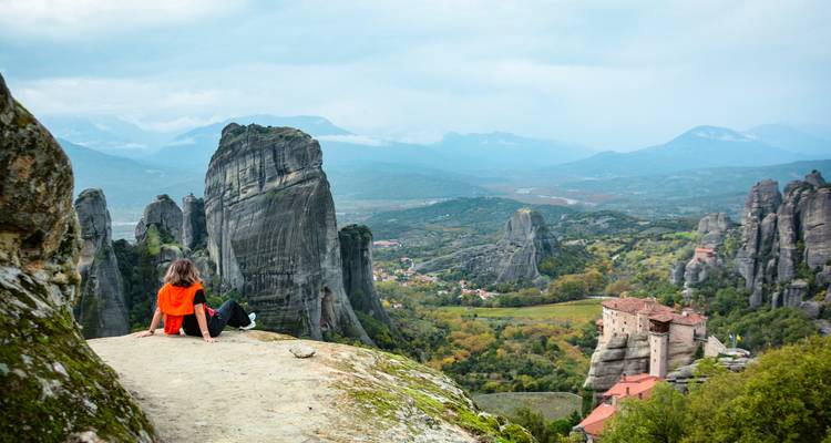 Traveller sits on a rock admiring the expansive Meteora valley dotted with monasteries