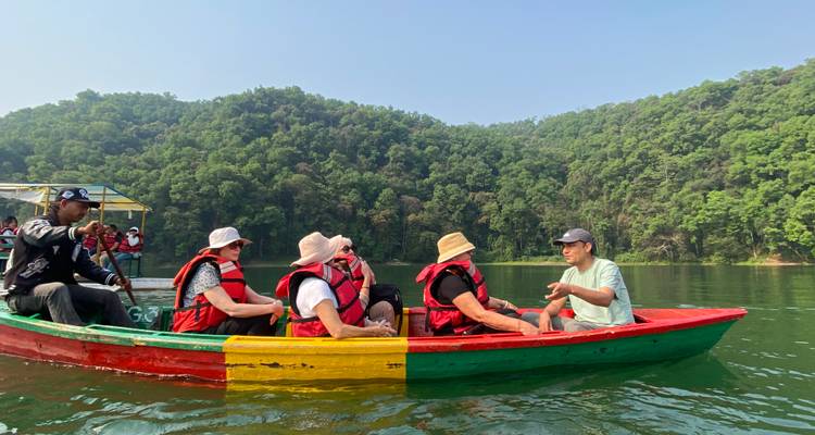 Les touristes vêtus de gilets de sauvetage pagaient sur un lac vert et calme dans un bateau en bois multicolore entouré de collines boisées.