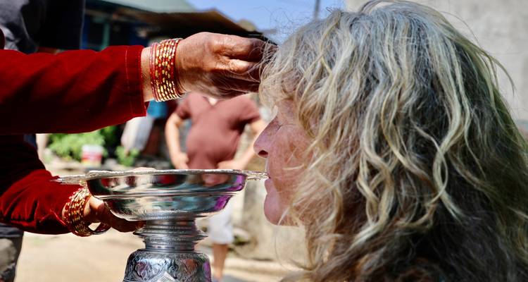 Un hôte local applique un tikka au front à une visiteuse blonde lors d'une cérémonie de bénédiction traditionnelle en plein air.