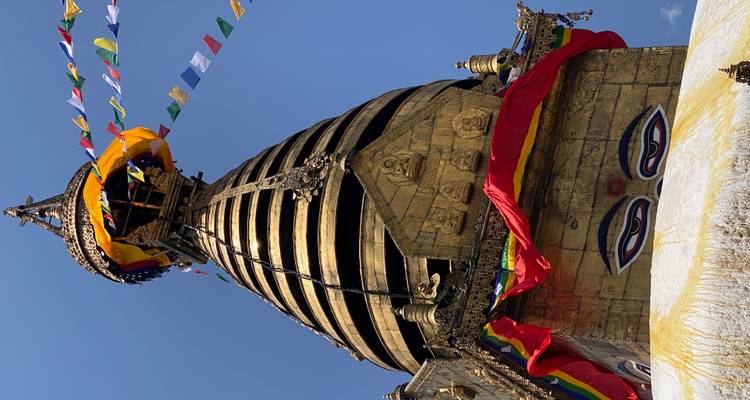 Flèche dorée du Stupa de Swayambhunath drapée de drapeaux de prière contre un ciel bleu clair de Katmandou.
