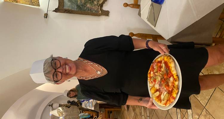 Femme souriante en toque de chef présentant une pizza personnelle fraîchement cuite à l'intérieur d'une trattoria confortable.