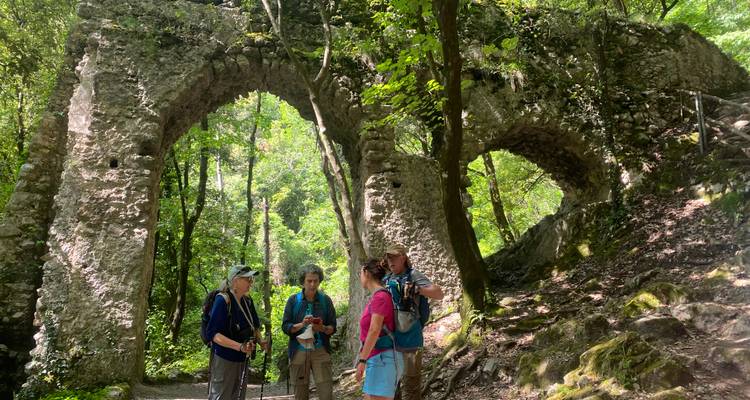 Les randonneurs font une pause sous des arches de pierre recouvertes de mousse dans une gorge forestière luxuriante, en étudiant une carte.