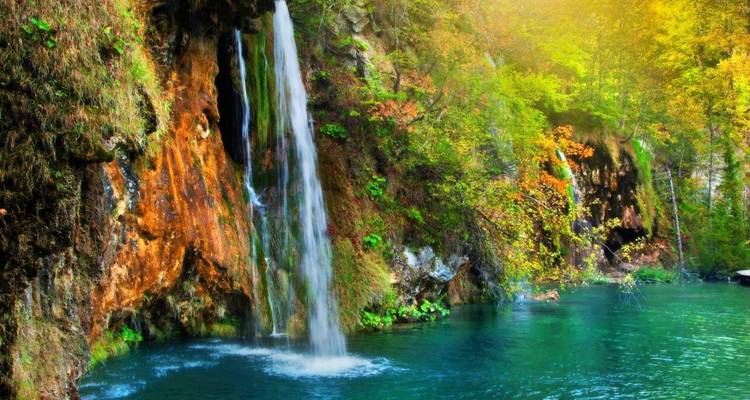 Lebhafter Wasserfall stürzt in einen smaragdgrünen Pool, umgeben von Herbstlaub in den Plitvicer Seen