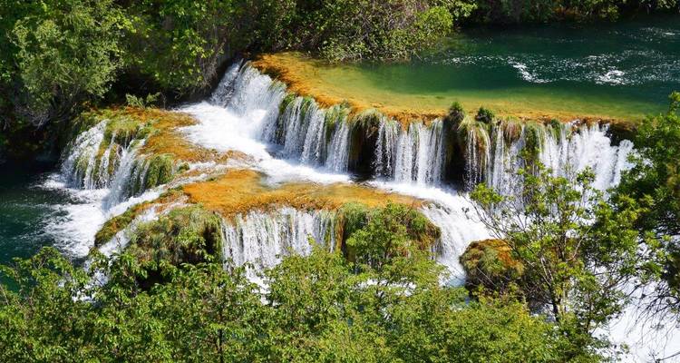 Draufsicht auf breite Wasserfälle über moosbedeckten Felsen im Nationalpark Krka mit grünem Wasser