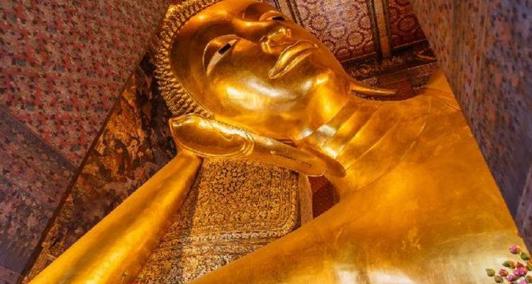 Primer plano de la estatua dorada del Buda Reclinado rodeada de paredes con patrones ornamentales en Wat Pho.