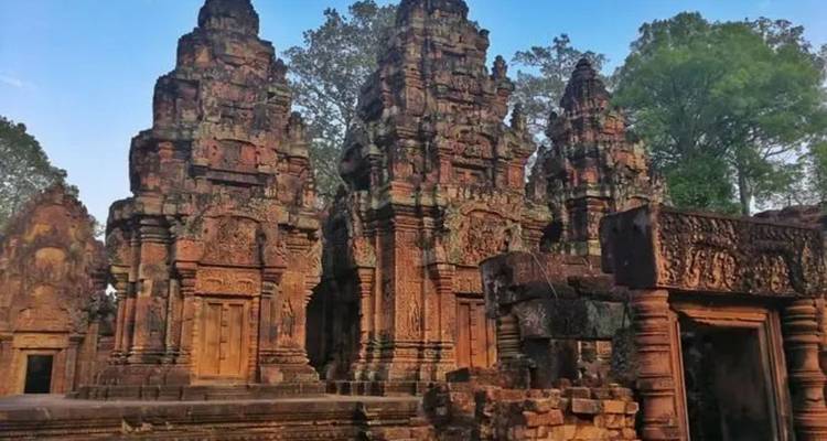 Torres de arenisca roja talladas con intrincados detalles del templo Banteay Srei rodeadas de árboles altos.