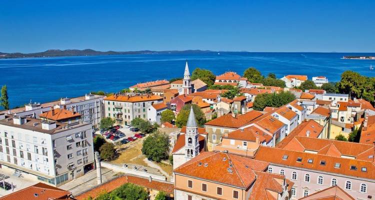Helderblauwe kustplaats in Kroatië met rode pannendaken die uitsteken in de diepblauwe zee op een zonnige dag