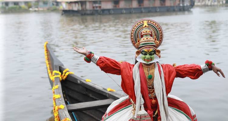 Bailarín de Kathakali completamente maquillado posando en una canoa decorada con flores en las aguas de Kerala.