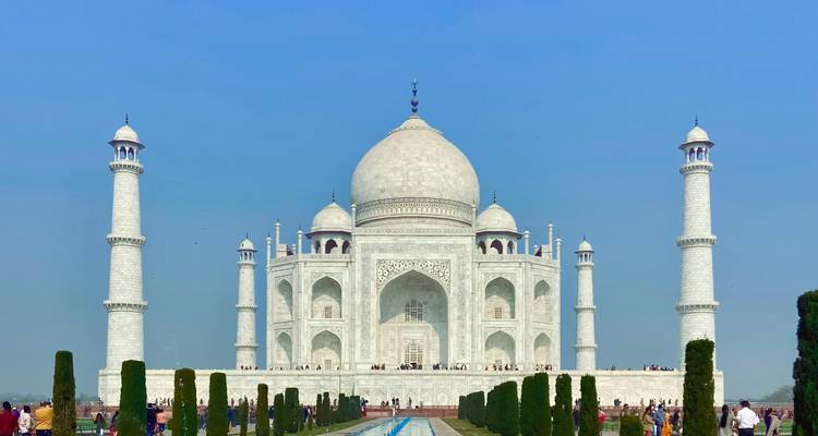 Iconisch frontaal uitzicht op het glimmende witte Taj Mahal omlijst door cipressenbomen en een turquoise weerspiegelend bassin.