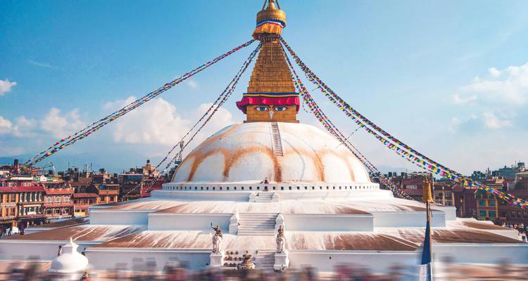 Le dôme blanc étincelant et la flèche dorée du Boudhanāth Stupa, ornés de drapeaux de prière, dominant les toits de Katmandou.