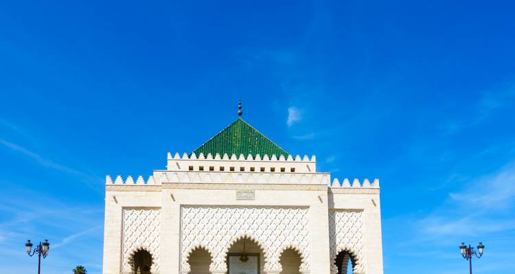 Le Mausolée blanc en marbre de Mohammed V avec son toit en pyramide verte se dresse isolé sur un vaste ciel bleu.