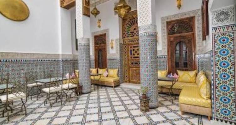 A traditional Moroccan riad courtyard decorated with intricate zellige tiles, carved wood and cushioned seating.