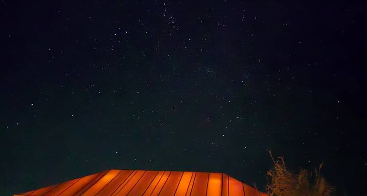 A dark night sky filled with faint stars above a softly lit desert tent roof.