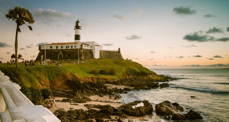 Historischer Leuchtturm auf einem grasbewachsenen Vorgebirge mit Blick auf felsige Küste bei Einbruch der Dunkelheit in Salvador.