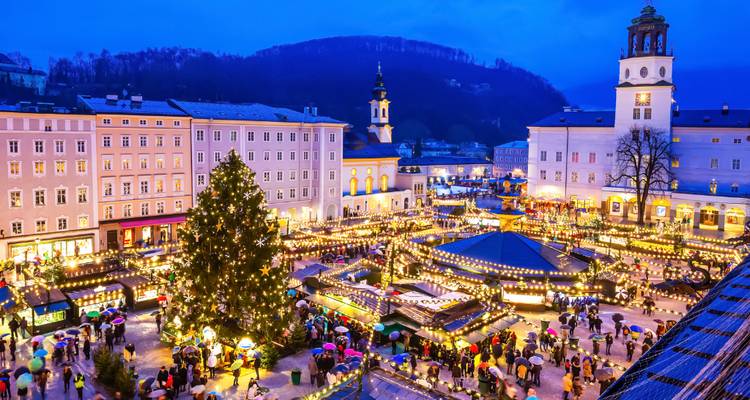 Luftaufnahme des Hauptplatzes von Salzburg, beleuchtet durch hunderte Weihnachtsstände und einen aufragenden Baum.