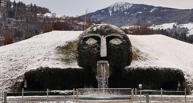 Der grasbewachsene Riesenkopf-Brunnen in der Swarovski Crystal Worlds mit verschneiter Alpinen Kulisse.