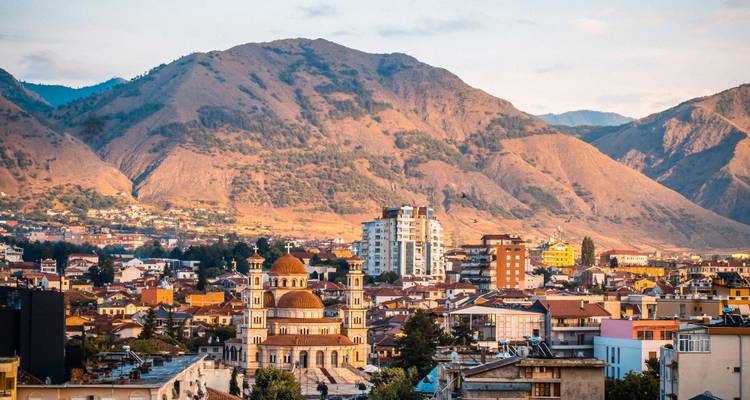 Vista panorámica de Korçë con una catedral de cúpula situada debajo de montañas escarpadas a la hora dorada.