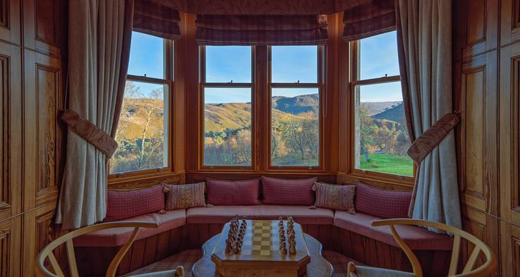 Rincón elegante con asientos junto a la ventana saliente con tablero de ajedrez que da a colinas boscosas y valle.