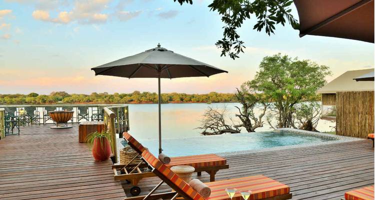 Luxury deck with loungers and infinity pool overlooking tranquil river at dusk