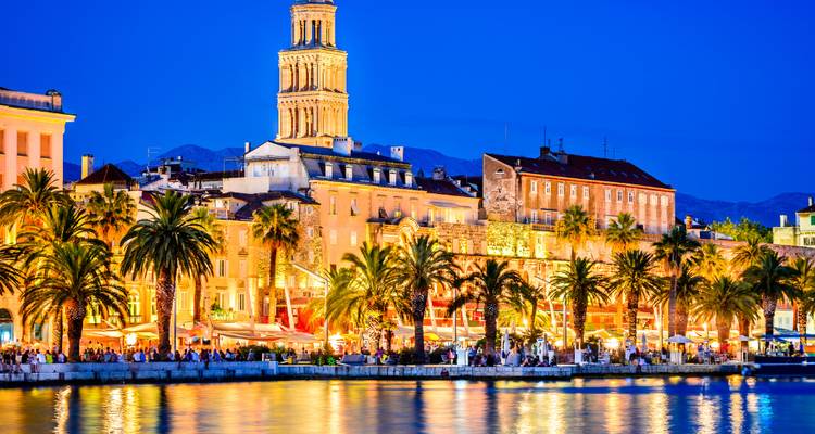 La promenade maritime de Split illuminée par des lumières chaleureuses à l'heure bleue se reflétant sur une eau calme.