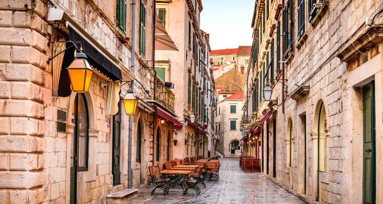 Ruelle en pierre étroite et charmante dans la vieille ville de Dubrovnik, bordée de tables de café en plein air et de lanternes.