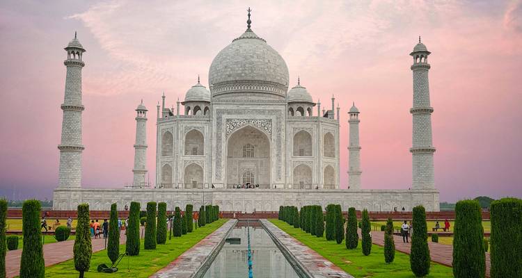 Das Taj Mahal, umrahmt von vier Minaretten bei Sonnenuntergang, spiegelt sich im langen Becken und den Gärten wider.
