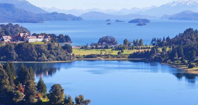 Lac vaste avec de petites péninsules et une ville alpine se dressant face aux pics enneigés lointains.