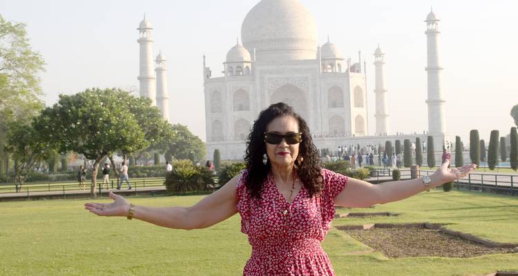 Frau im roten Kleid posiert mit ausgestreckten Armen vor dem verschwommenen Taj Mahal.