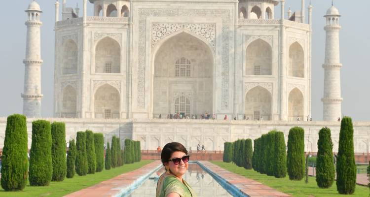 Lächelnde Frau im grünen Sari steht neben einem Spiegelteich mit dem makellosen Taj Mahal im Hintergrund.