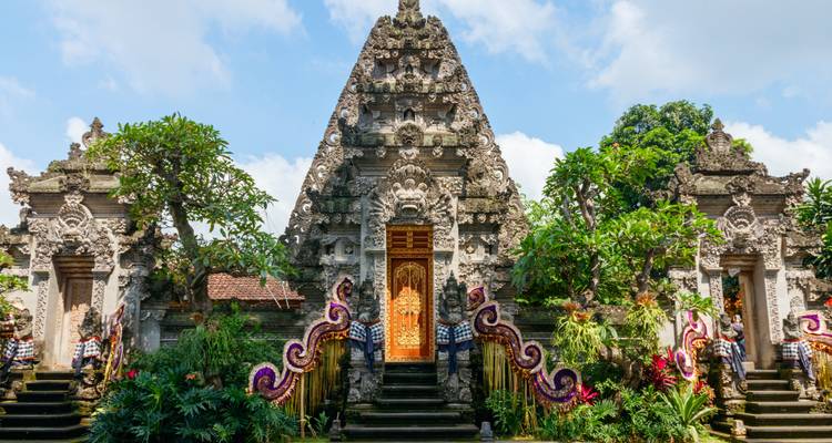Ingewikkeld gesneden stenen ingang van een Balinese tempel omringd door tropische begroeiing.