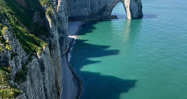 Les dramatiques falaises blanches de craie et l'arche naturelle d'Étretat plongent dans une mer turquoise, projetant des ombres frappantes.