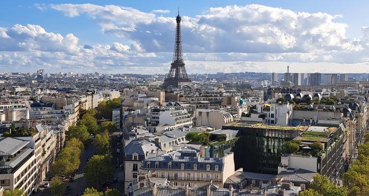 Vue panoramique des toits de Paris avec la Tour Eiffel se dressant contre un ciel parsemé de nuages floconneux.