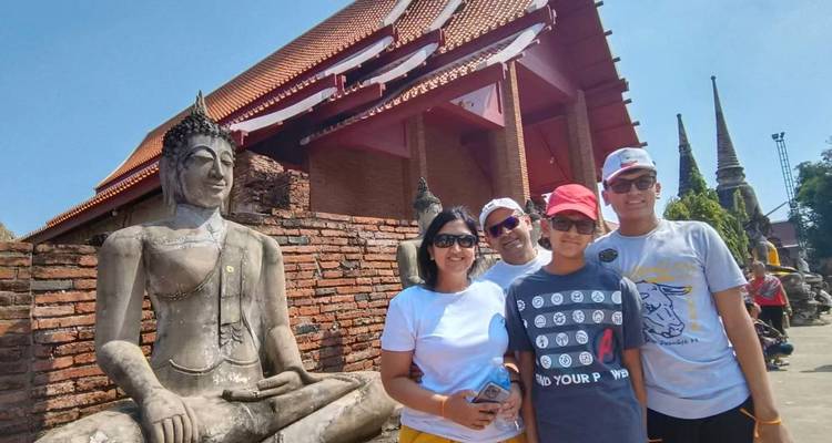 Un groupe familial pose à côté d'une statue de Bouddha assis et d'un chedi en briques dans un site de temple thaïlandais baigné de soleil.