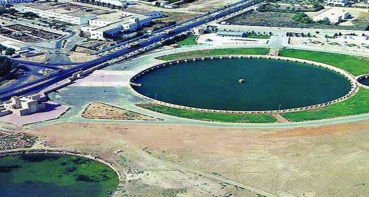 Aerial view of a massive circular water reservoir surrounded by arid terrain and urban streets.