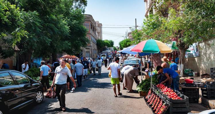 Lively street market packed with shoppers, colourful umbrellas and fresh produce stalls.
