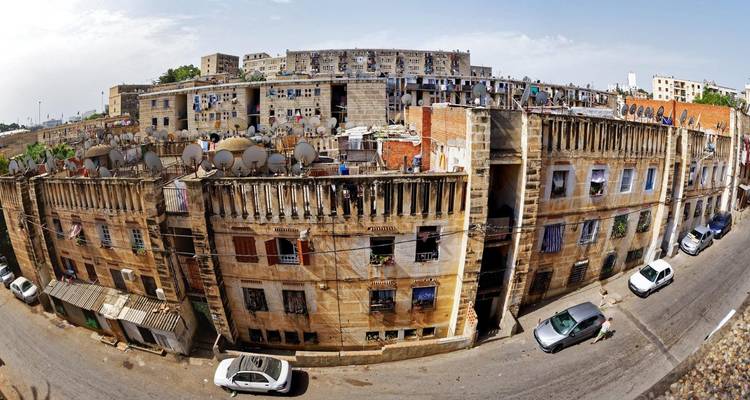 Panoramic fisheye view of aged apartment blocks laden with satellite dishes along a narrow street.