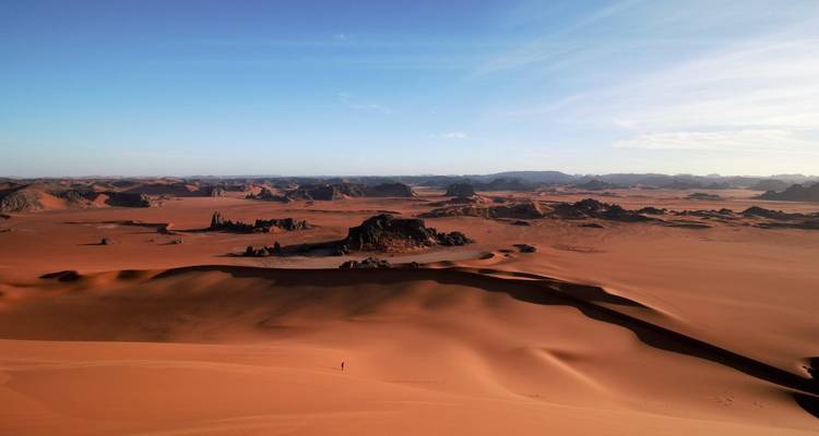 Vast red-sand desert dotted with dramatic rock formations under a clear blue sky.