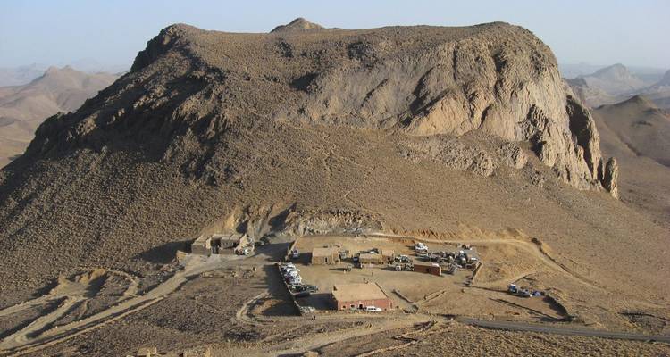 Rocky mountain rises above a small remote base camp and winding desert tracks.