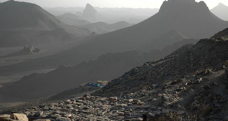 Moody, rugged mountain silhouettes and stone trail descending into a hazy desert valley.