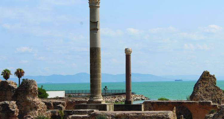 Two ancient Roman columns rise above seaside ruins overlooking turquoise Mediterranean waters.
