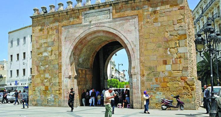 Stone gate Bab El Bhar frames a bustling plaza with locals and visitors in Tunis.