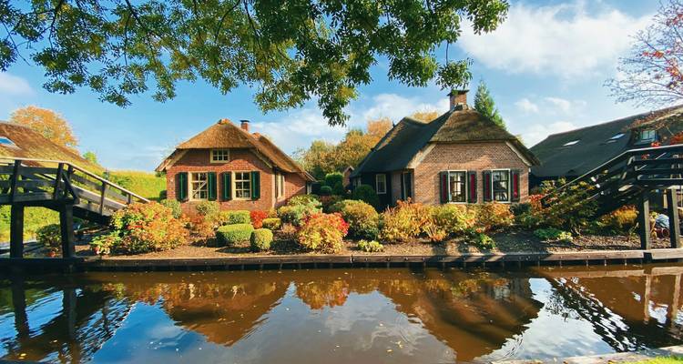 Malerische Backsteinhäuschen mit gestutzten Hecken, die sich in einem ruhigen Giethoornkanal an einem Herbstmorgen spiegeln.