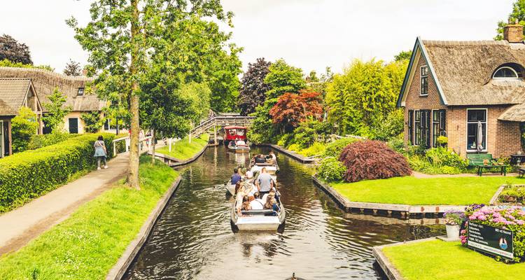 Canal estrecho en Giethoorn con pequeños botes pasando entre jardines verdes y puentes de madera.