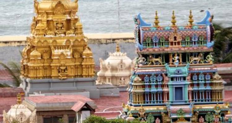 Colorful shrine towers overlooking the sea with rooftops in the foreground.