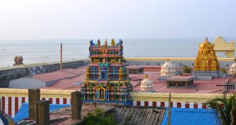 Temple complex with colorful towers beside the ocean under a pale sky.
