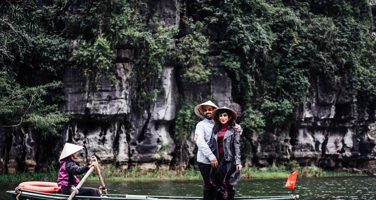 Les touristes portant des chapeaux coniques posant sur un petit bateau avec des falaises couvertes de jungle derrière eux à Ninh Binh.