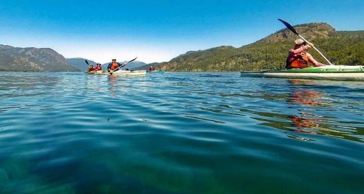 Plusieurs kayaks glissent sur les eaux cristallines d'un lac bleu-vert sous un ciel d'été radieux.