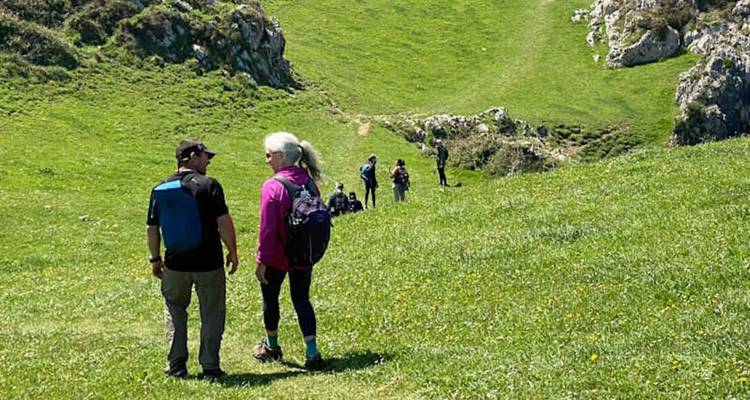 Excursionistas caminando por una colina verde cubierta de pasto con afloramientos rocosos bajo la luz clara del día